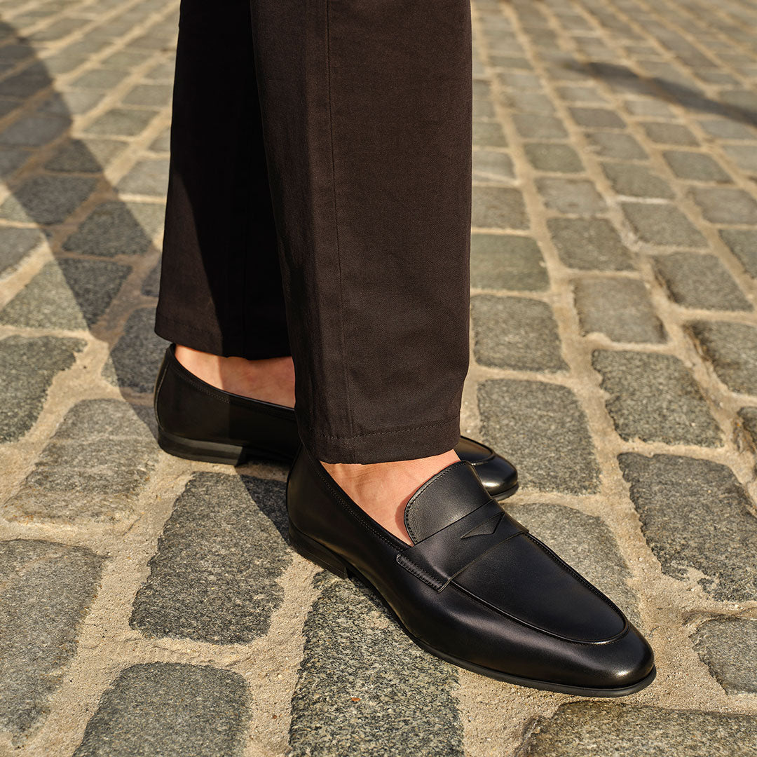 Man in a black pants wearing To Boot's Keats Black Calf Leather Loafer standing on a cobblestone street.